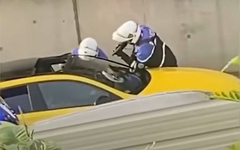 Les deux policiers sont contre un muret, appuyés sur la voiture, avec leurs équipements de motards, gants compris