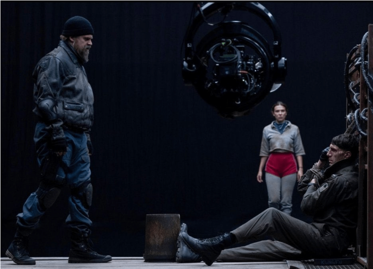 Dans cette image de tournage révélée par le magazine Empire, on peut voir Hopper confronter un homme qui semble faire partie de cette fameuse unité spéciale, ligoté, probablement après un combat intense, pendant que Eleven (qui semble ne pas être physiquement présente), observe la scène.